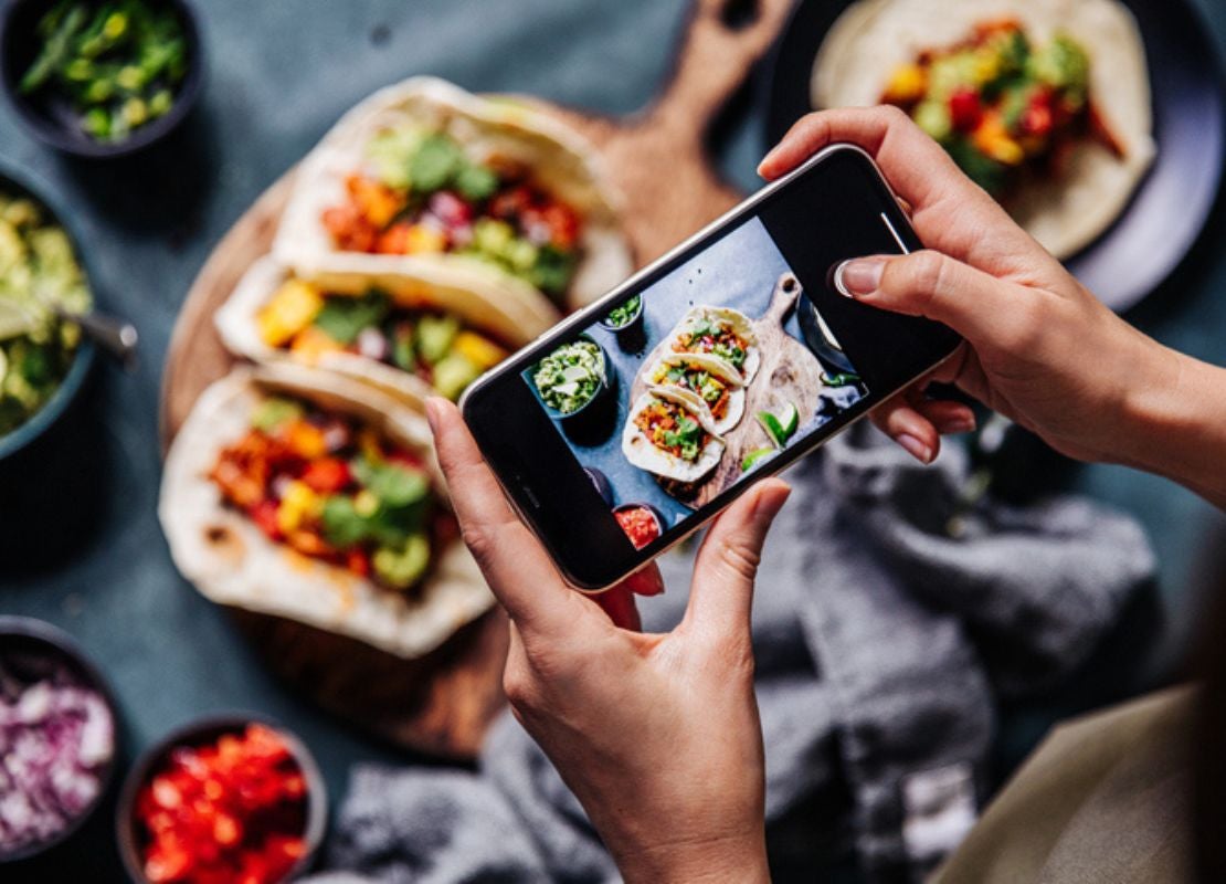 Blogger gastronómico toma foto de tacos y sus ingredientes con celular para redes sociales.