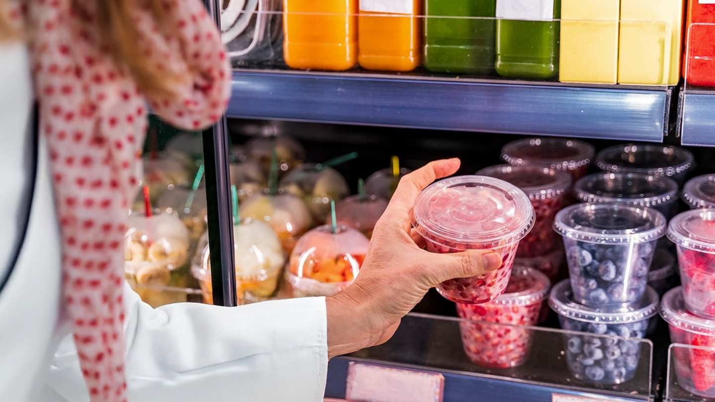 Persona revisa envase con frutas en refrigerador, ejemplo de etiquetado de alimentos.