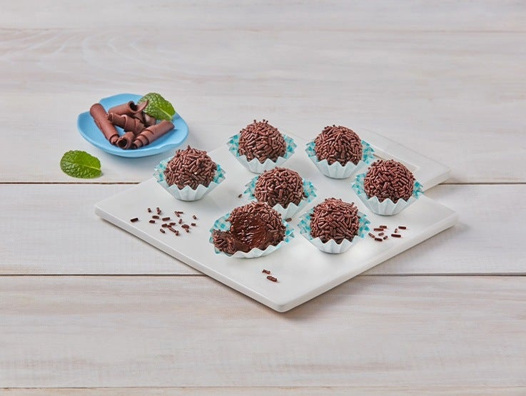 Trufas de chocolate cubiertas con grageas sobre base blanca y decoración de cacao