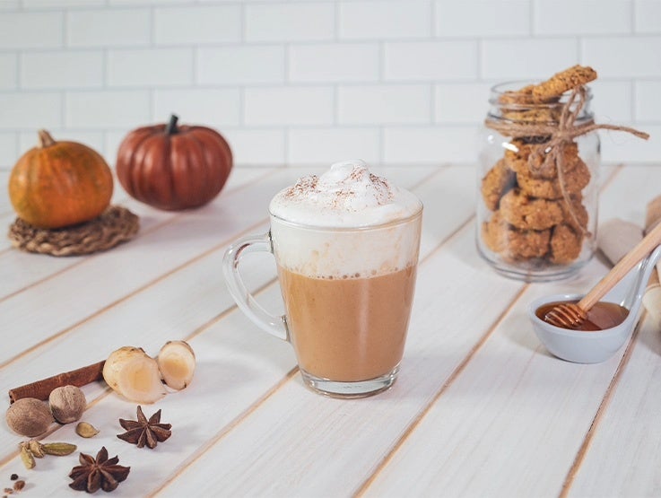 Bebida caliente de chocolate con crema y especias servida en vaso sobre mesa clara
