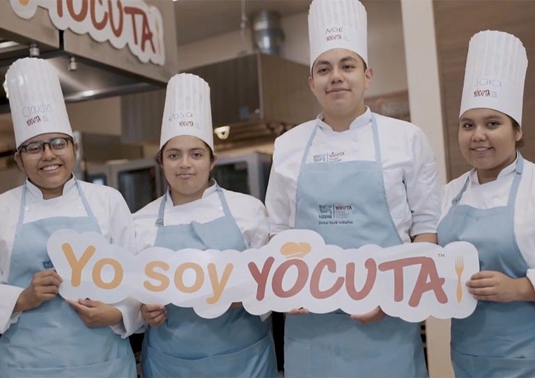 Grupo de jóvenes cocineros con uniforme sosteniendo un letrero de Yo soy YOCUTA