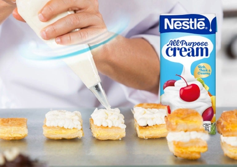 Chef salteando y otro decorando con una manga pastelera junto a NESTLÉ® en una cocina profesional