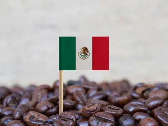 Bandera de México sobre granos de café tostado, representando origen y calidad del producto