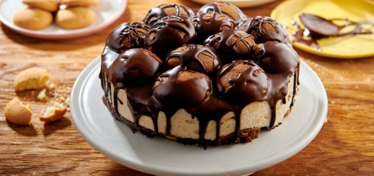 Pastel de chocolate sobre soporte de repostería y un muffing de chocolate acompañando
