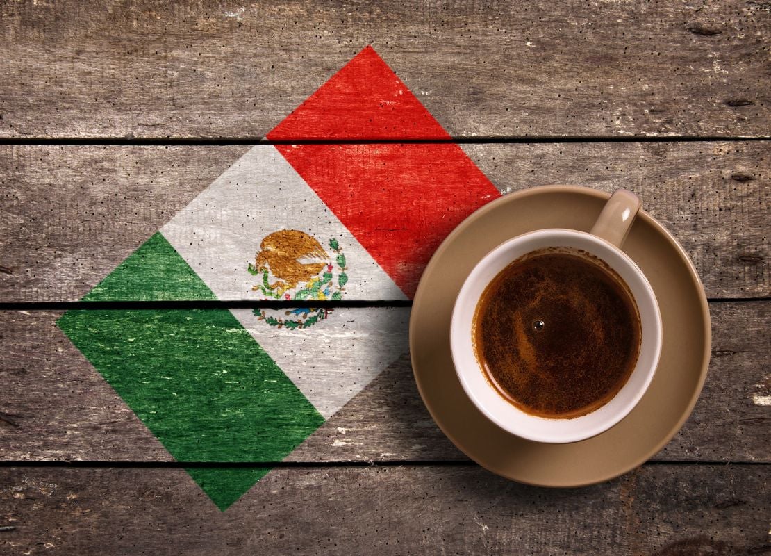 Taza de café junto a una bandera de México pintada sobre madera rústica