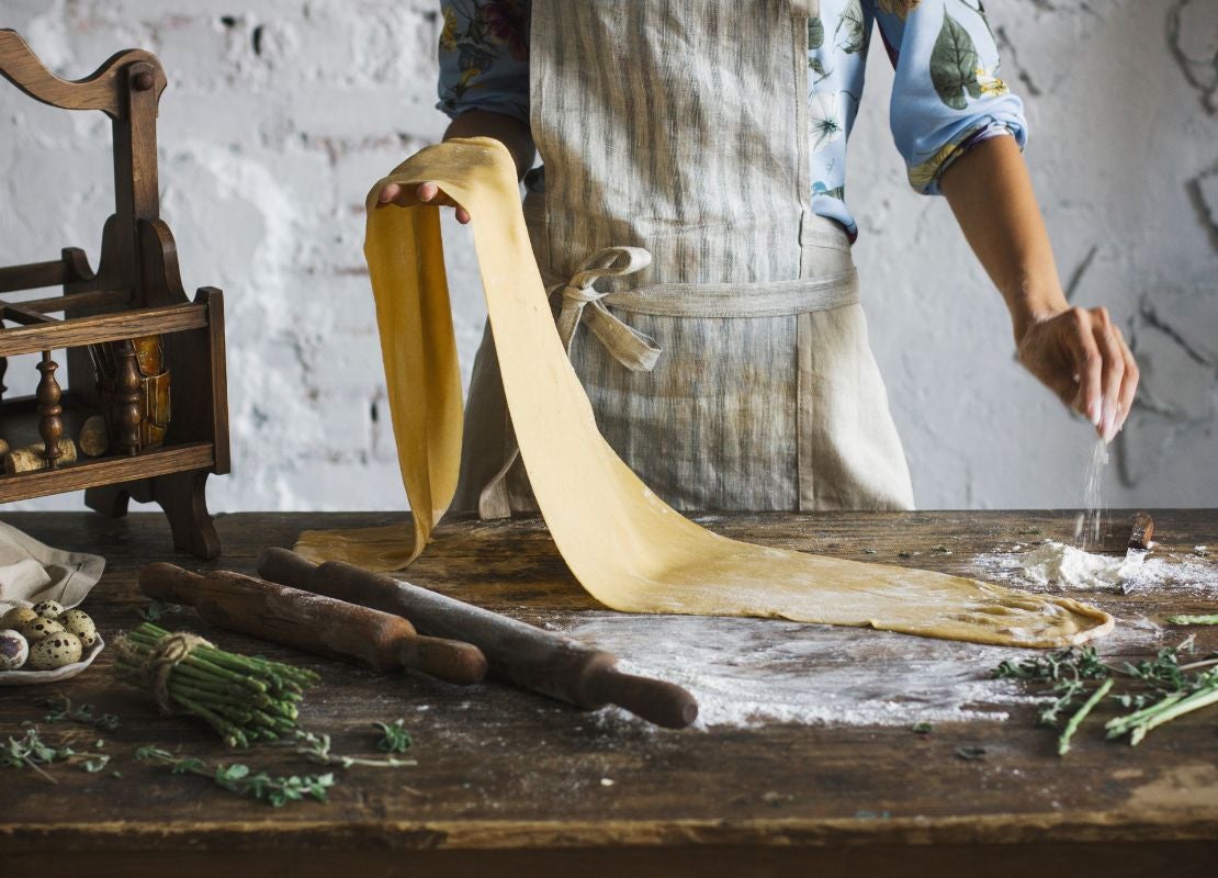 Persona estirando masa sobre mesa con utensilios y harina para elaborar pasta de la cocina italina
