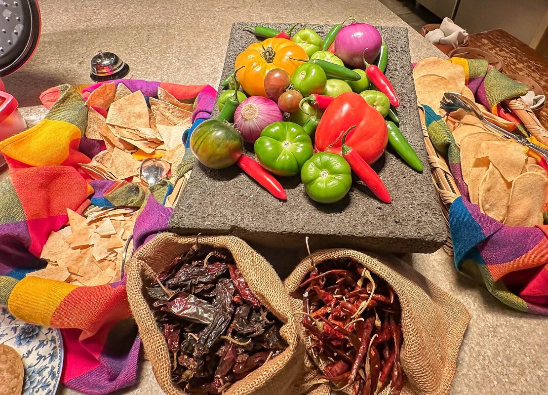Ingredientes frescos como chiles, tomates y tortillas sobre mesa con textiles coloridos