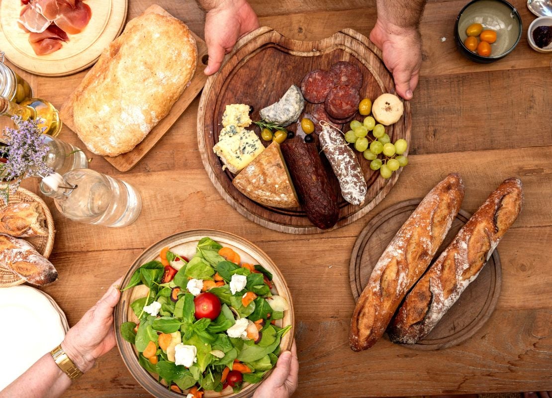Tabla con quesos, embutidos, pan y frutas sobre mesa de madera vista superior