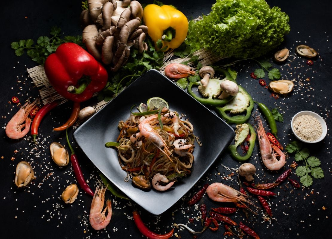 Plato con fideos, camarones y vegetales rodeado de ingredientes frescos