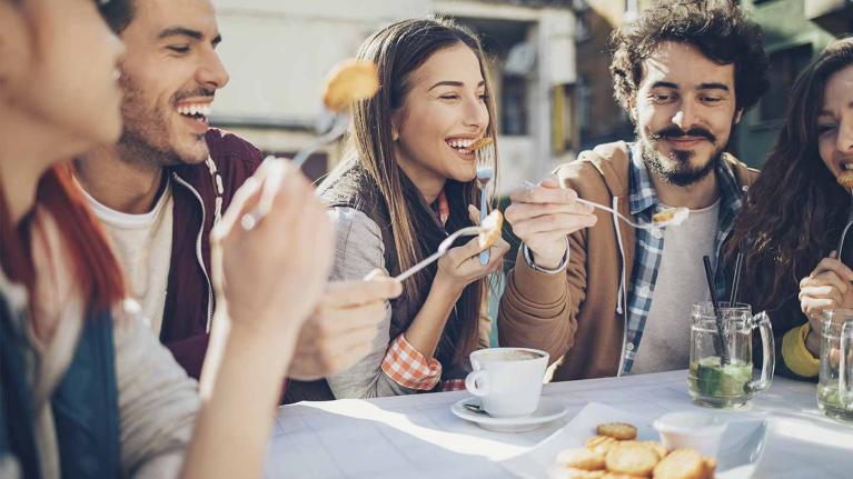 Cinco comensales emocionados disfrutan al aire libre algunos bocadillos y bebidas en la mesa de un restaurante 