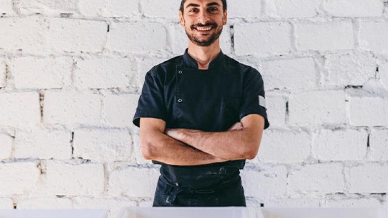 Emprendedor gastronómico sonriendo con los brazos cruzados frente a cestas de masas para panadería