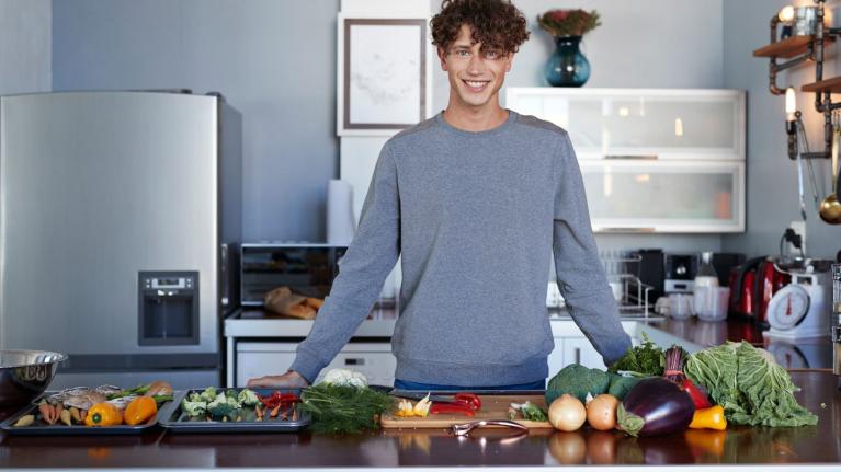 Persona frente a una mesa con vegetales frescos, lista para ofrecer una experiencia culinaria virtual desde la cocina