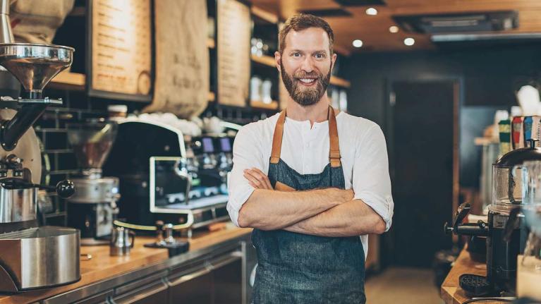 Barista sonriendo con los brazos cruzados tras el mostrador de en una cafetería