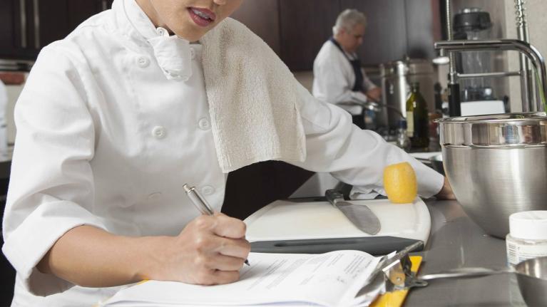 Chef revisa documentos en cocina profesional para identificar cuellos de botella en la operación. 