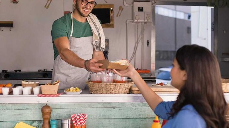 Emprendedor atiende clientes en food trucks ofreciendo comida rápida desde una cocina móvil.