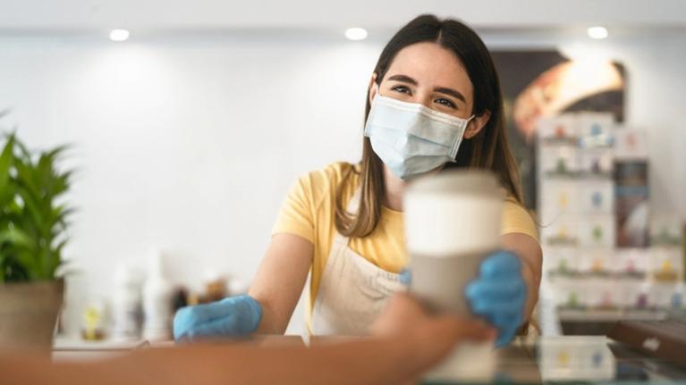 Trabajadora con mascarilla entrega una bebida como parte del servicio de alimentos en hospitales.