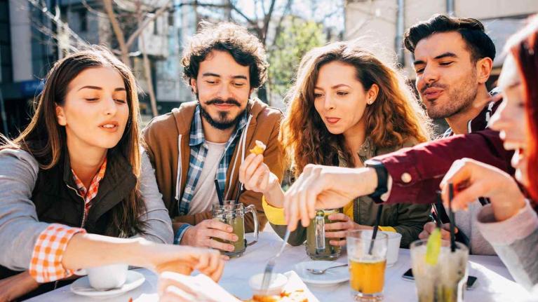 Grupo de millennials comparte comida y bebidas al aire libre, representando distintos tipos de consumidores.