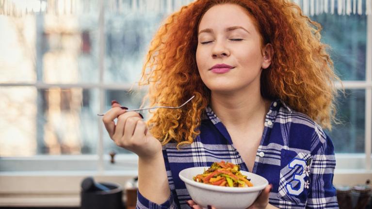 Mujer sostiene un bowl de comida y prueba con un tenedor con los ojos cerrados