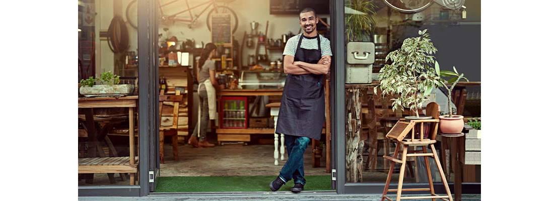 Hombre con mandil negro en la puerta de su cafetería