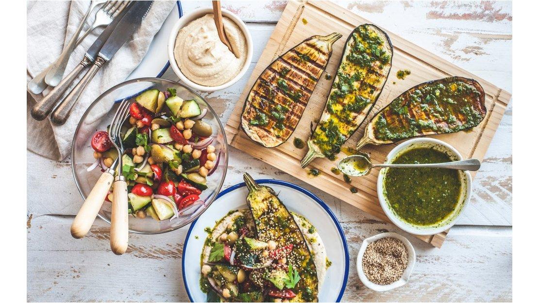 En plano cenital se arma un plato saludable con berenjenas, pesto y verduras con humus