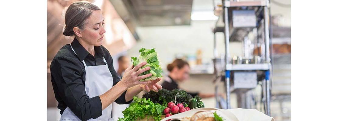 Mujer en cocina profesional con una lechuga en la mano alistando las verduras
