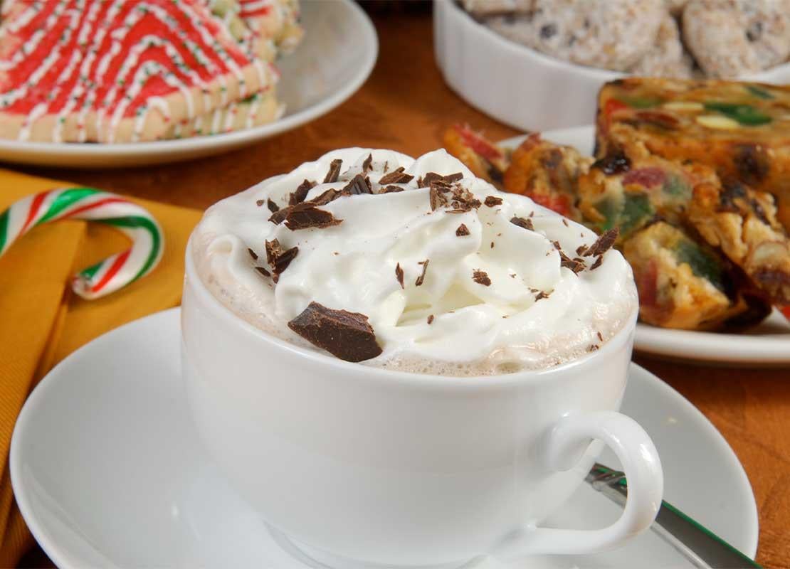 Una taza de cappuccino caliente con nata montada, tarta de frutas y postres navideños que hacen un buen maridaje