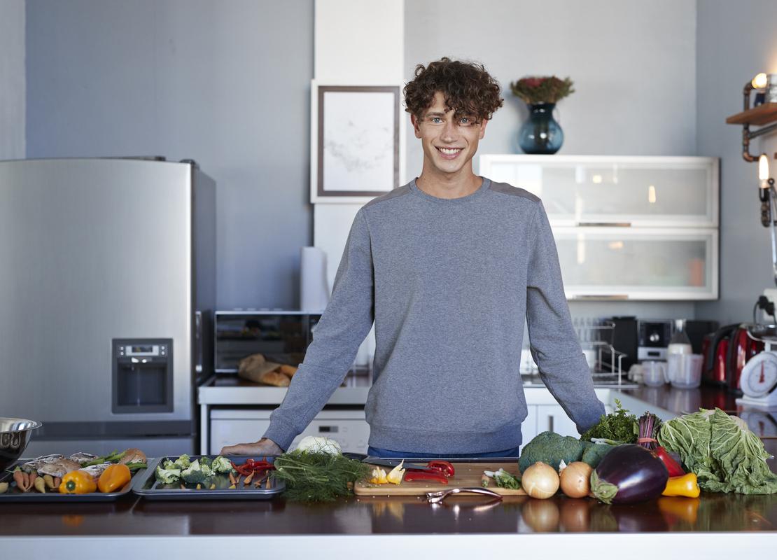 Detrás de una mesa con verduras, un influencer gastronómico mira al frente y se preparara para hacer un video en su cocina