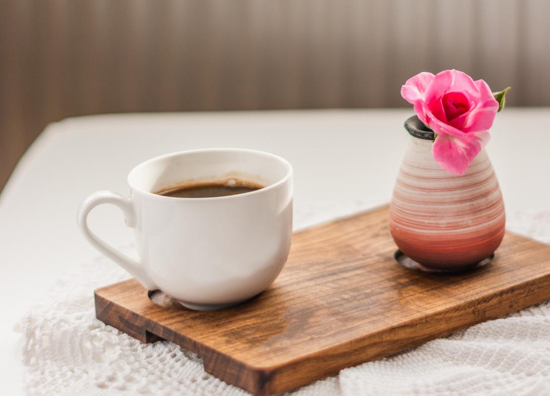 Sobre una tabla, una taza de café y una rosa en un jarrón como souvenir para obsequiar en el Día Internacional de la Mujer