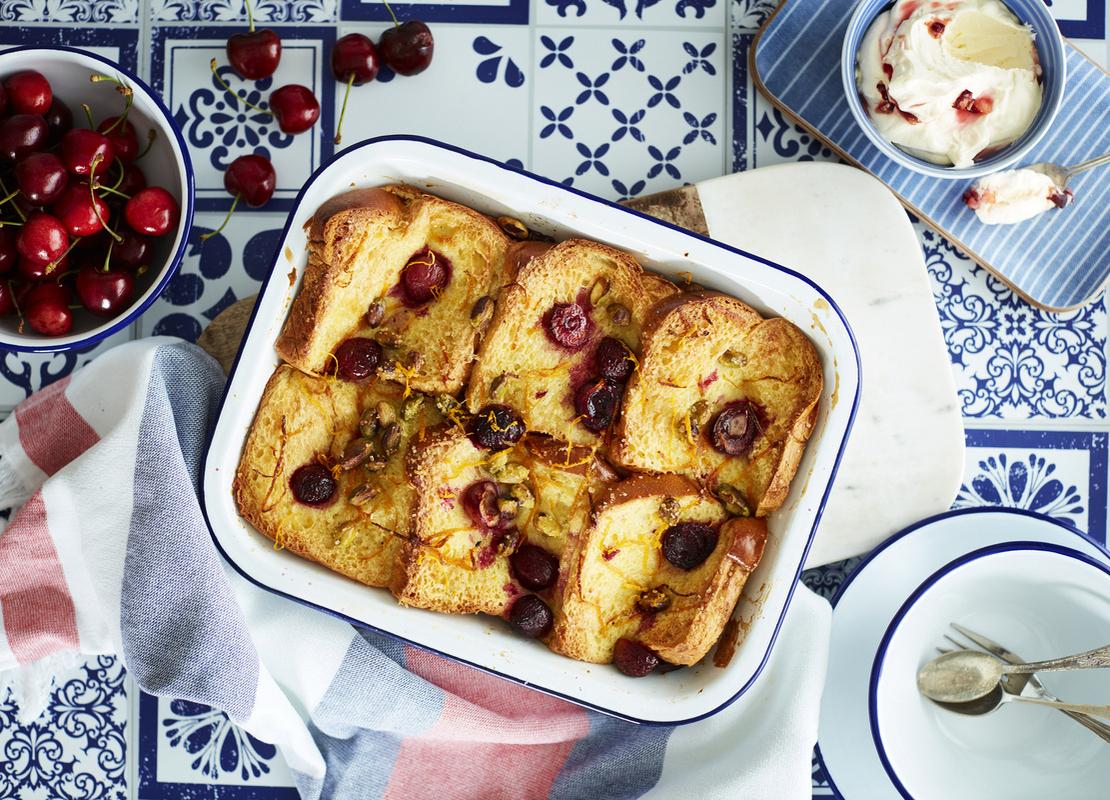 Bandeja de aluminio con 6 torrijas decoradas con fruta y mantequilla y alrededor una taza con cerezas y otra con helado