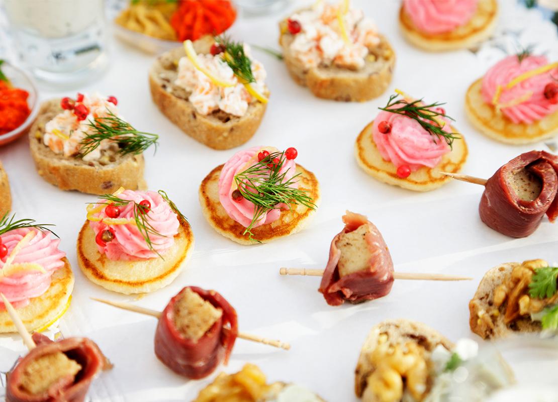 Diferentes tipos de postres y canapés coloridos en porción individual servidos sobre una mesa blanca