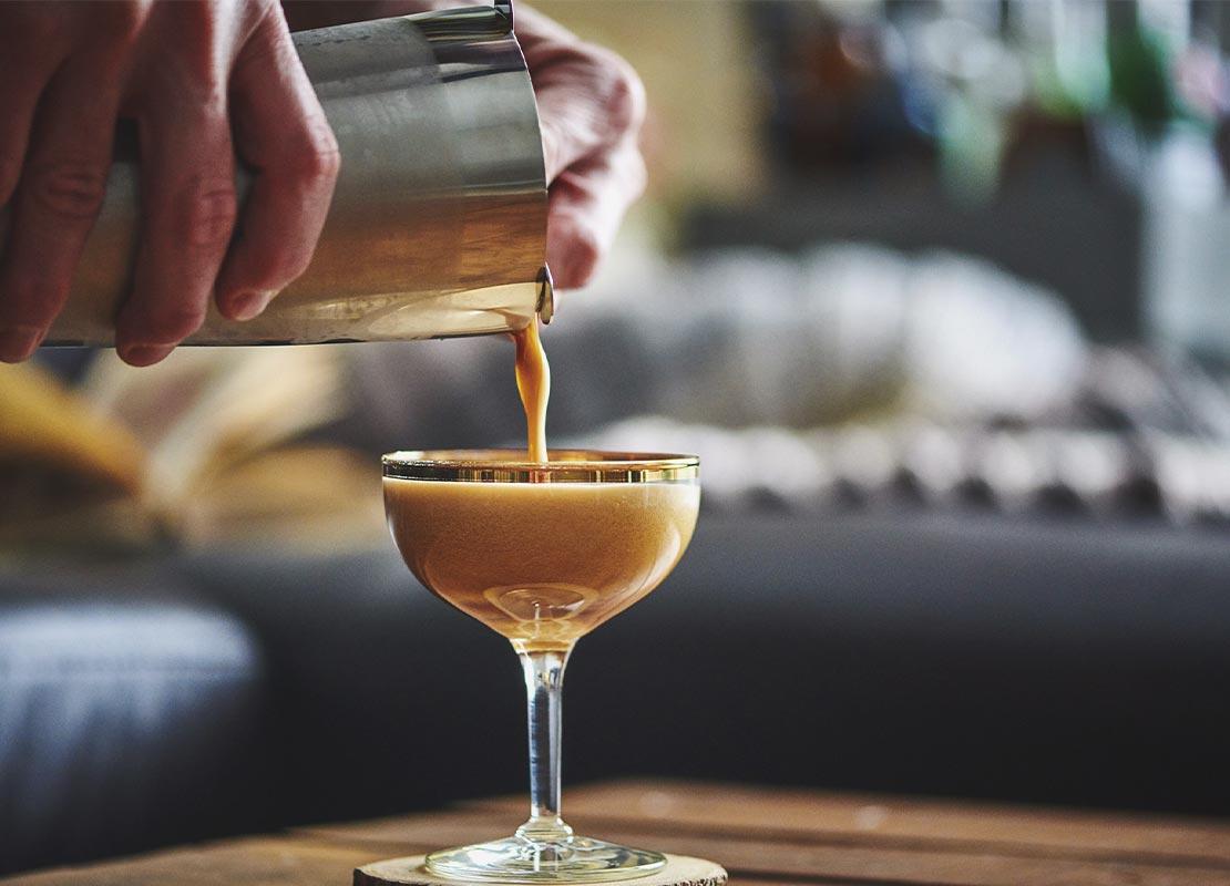 Manos masculinas sirven de una coctelera un cóctel espresso martini NESCAFÉ® en una copa