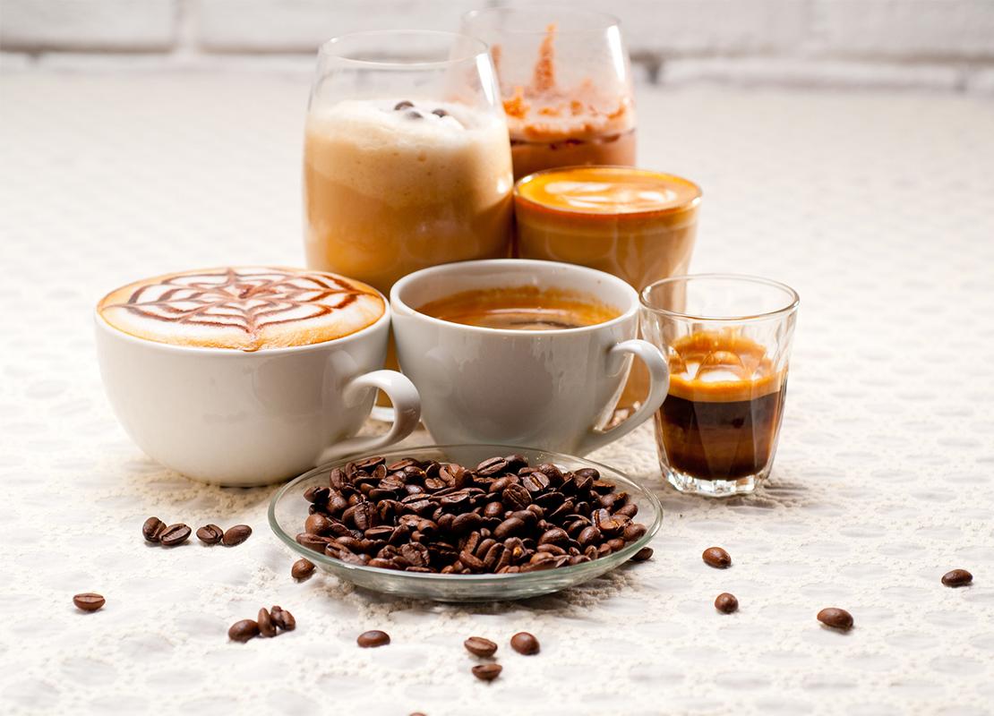 Un plato con granos de café tostados y al fondo seis tipos de bebidas como espresso, café frío, latte, entre otras