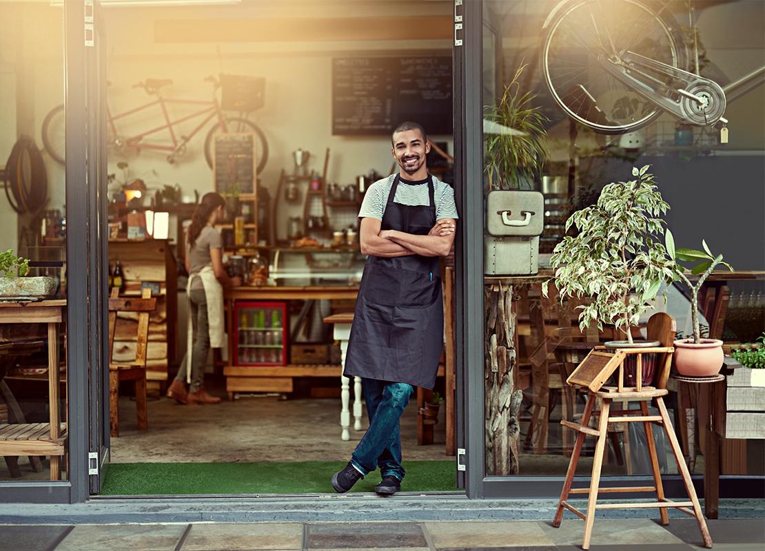 Barista apoyado en la puerta de una cafetería de estilo rústico, decorada con elementos naturales