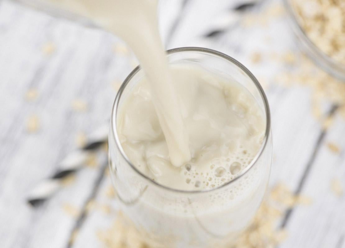 En un vaso sobre una mesa de madera se sirve bebida vegetal de avena