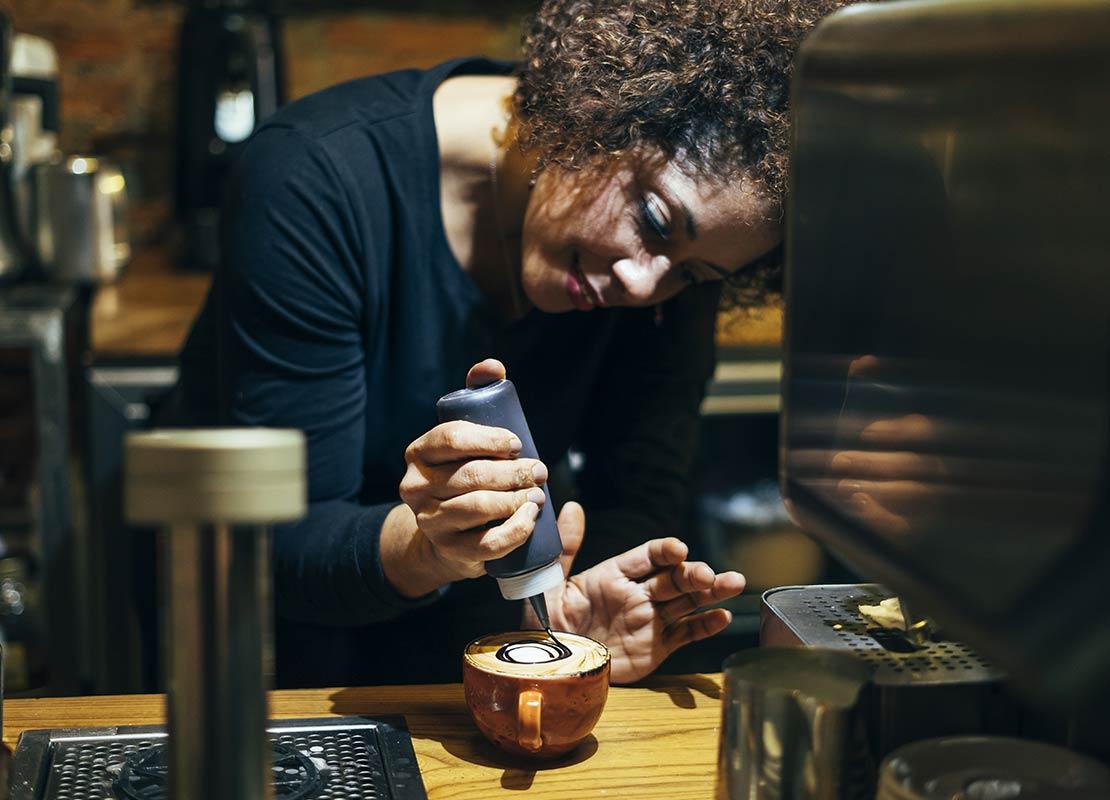 Barista decora con cuidado una bebida con un sirope de chocolate en una cafetería