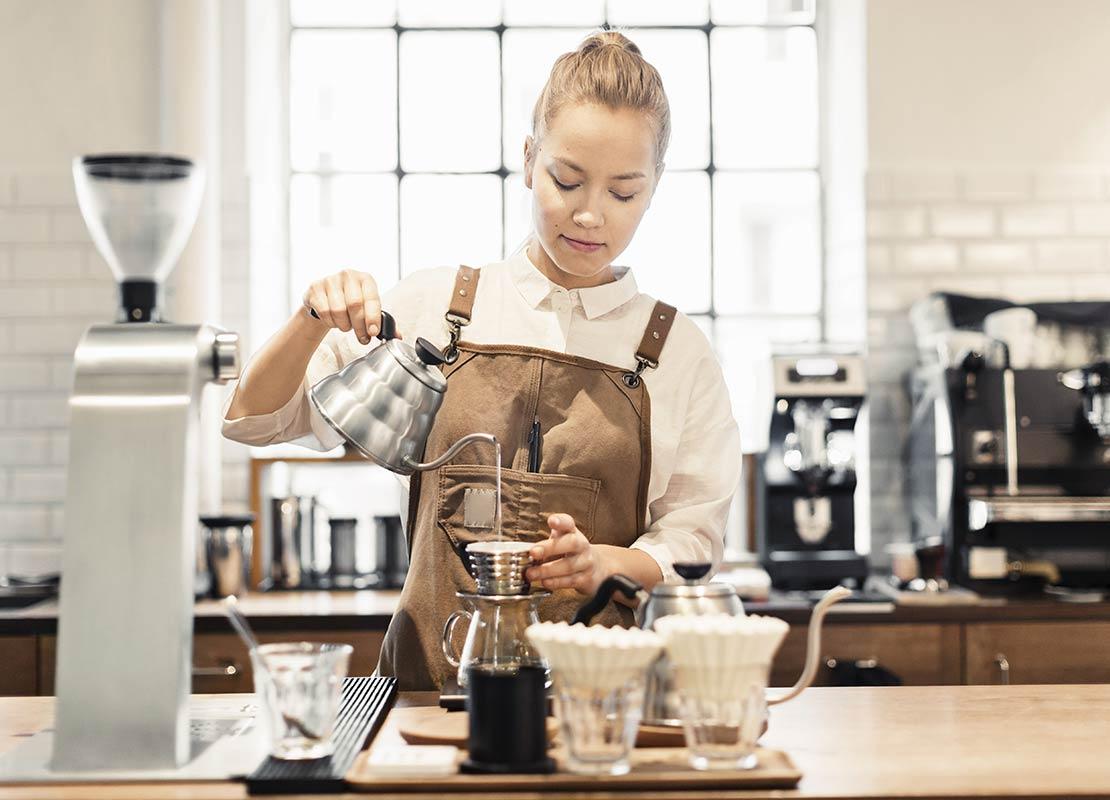 Barista utiliza herramientas como un dripper y tetera de agua caliente para preparar café filtrado