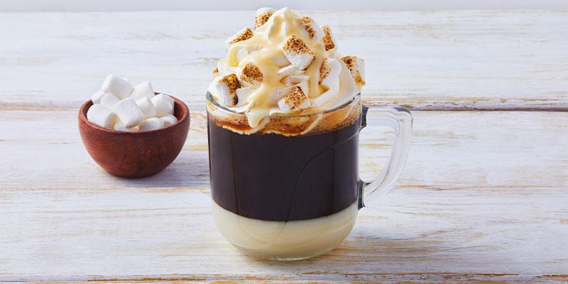 Taza blanca de café bombón decorado con crema batida, leche condensada y masmelos