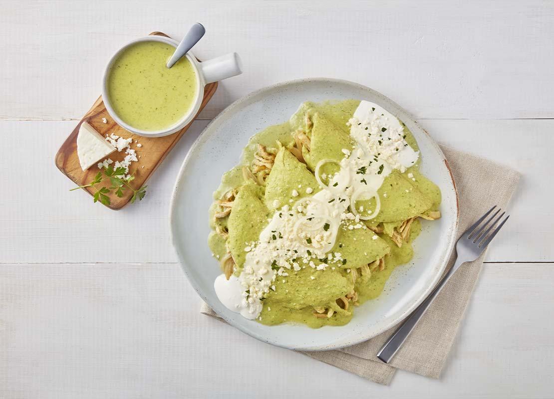 Plato de enchiladas cubiertas con crema verde elaborada con productos lácteos de CARNATION® CLAVEL®