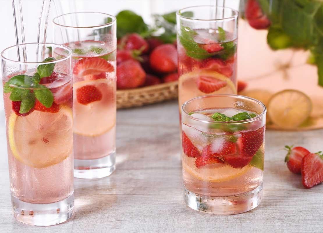 4 vasos de diferentes tamaños con agua saborizada de fresas, limones y hierba buena