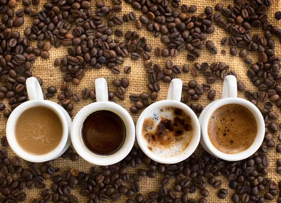 4 tazas con diferentes bebidas calientes rodeadas de granos de café tostado NESCAFÉ®