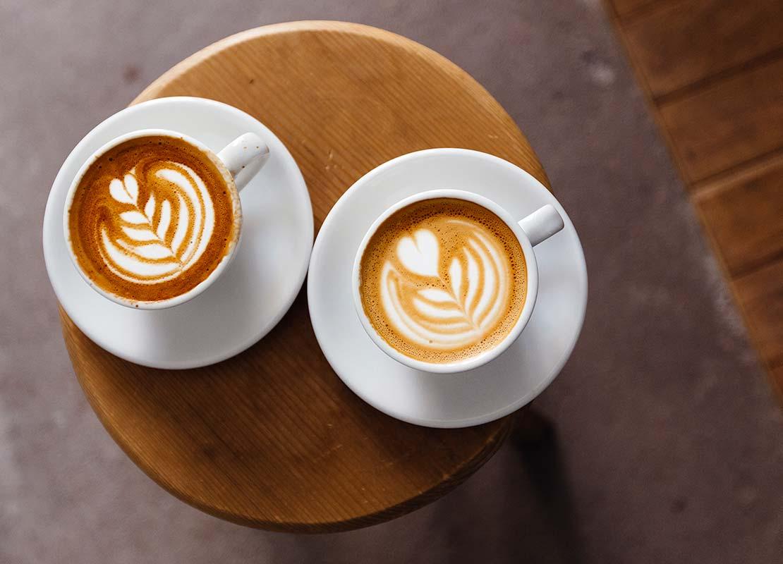 Dos tazas de cappuccinos NESCAFÉ® con latte art sobre una mesa pequeña de madera
