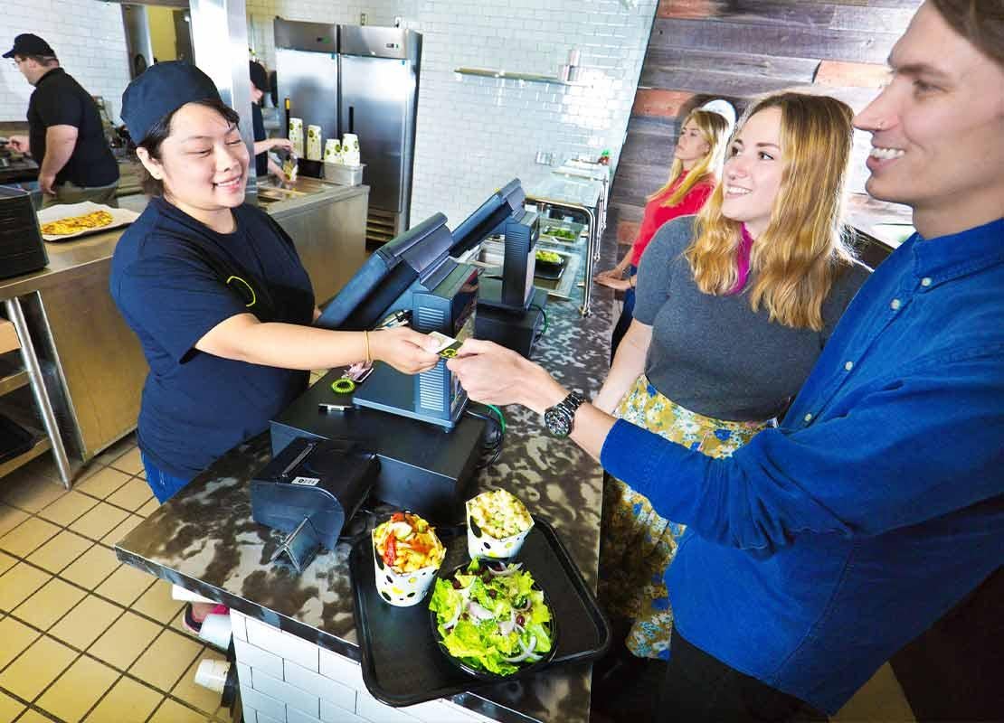 Cajera de un restaurante recibe la tarjeta de dos clientes que pagan su comida sobre el mostrador