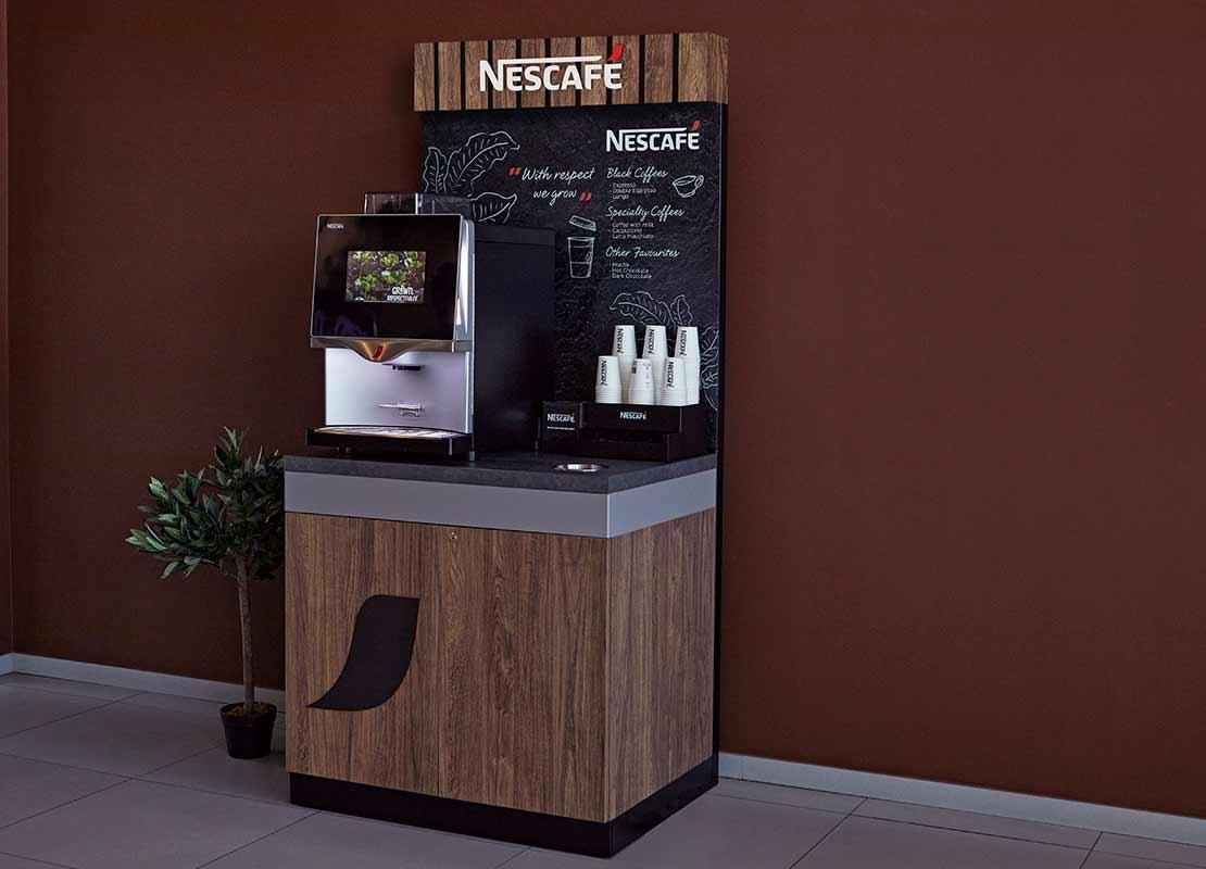 Mueble de madera sostiene una máquina NESCAFÉ®, vasos, tapas y material POP