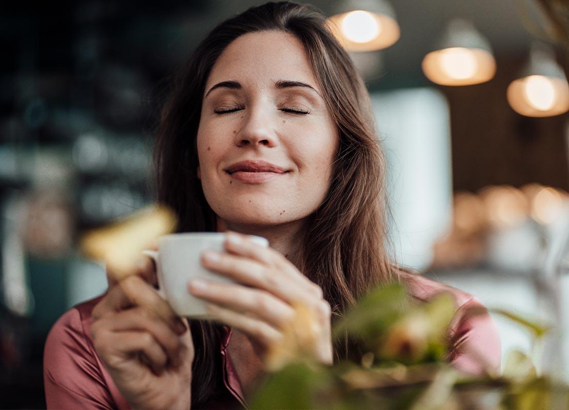Mujer disfruta con los ojos cerrados del aroma y sabor de una taza de café que sostiene en las manos