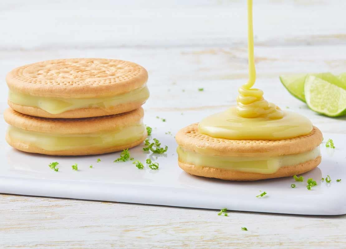 Sobre una tabla de cortar, galletas rellenas de crema de limón y sobre una cae leche condensada