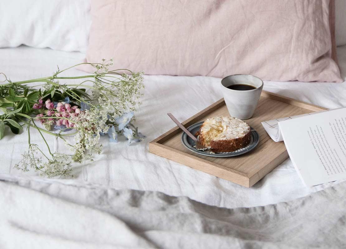 Bandeja con café y postre sobre una cama de la habitación de un hotel que tiene flores