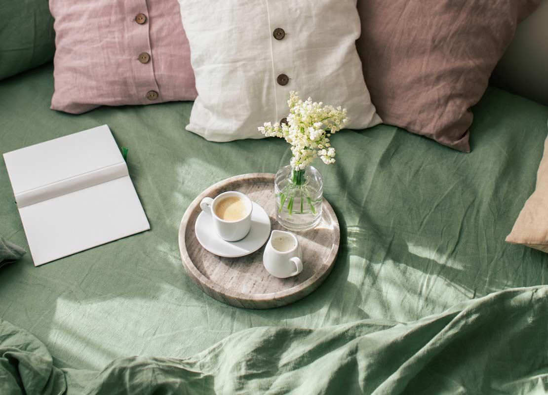 Cama de la habitación de un hotel con almohadas de colores y un servicio de café y leche sobre una bandeja