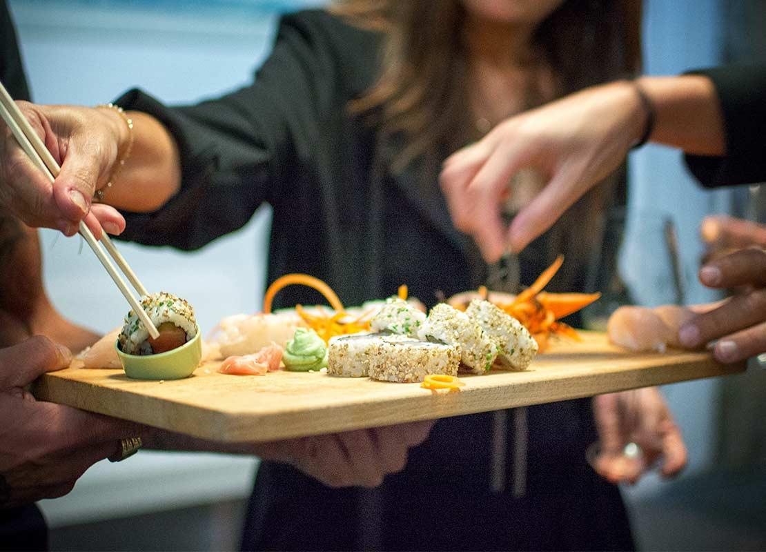 Mujer toma un maki con palillos de una tabla con sushi que un camarero sostiene en sus manos