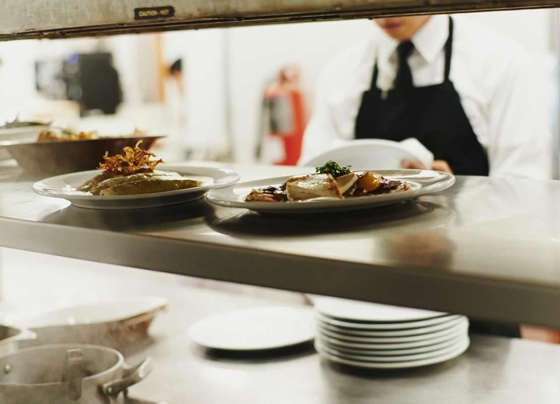 Platos servidos en el mostrador de una cocina, esperando a ser recogidos por el mesero del fondo
