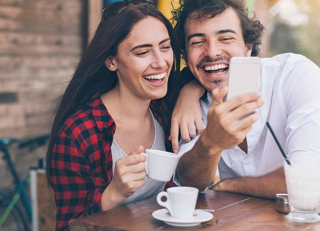 Pareja sentada a la mesa se toma una selfie mientras bebe café a las afueras de una cafetería